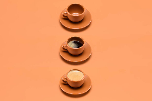 close up view of arrangement of empty cup and two cups of coffee isolated on peach