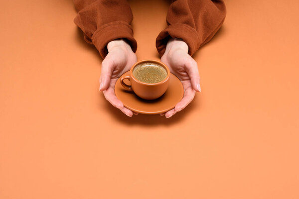 cropped shot of woman holding cup of coffee on saucer in hands isolated on peach