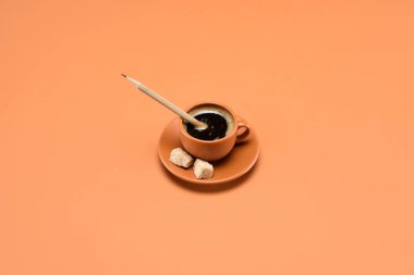close up view of cup of coffee with pencil and cane sugar on saucer isolated on peach clipart