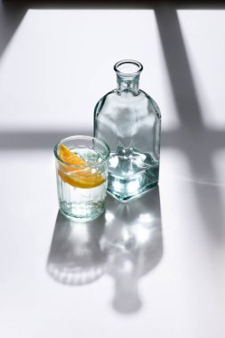 Beyaz yüzeyi su ile şişe ve cam limon parça ile görünümü kadar kapatın