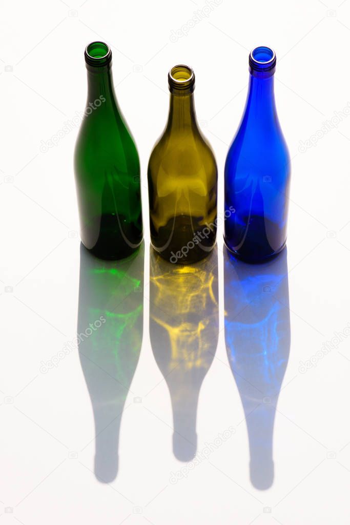 close up view of empty colorful glass bottles with shadows on white background