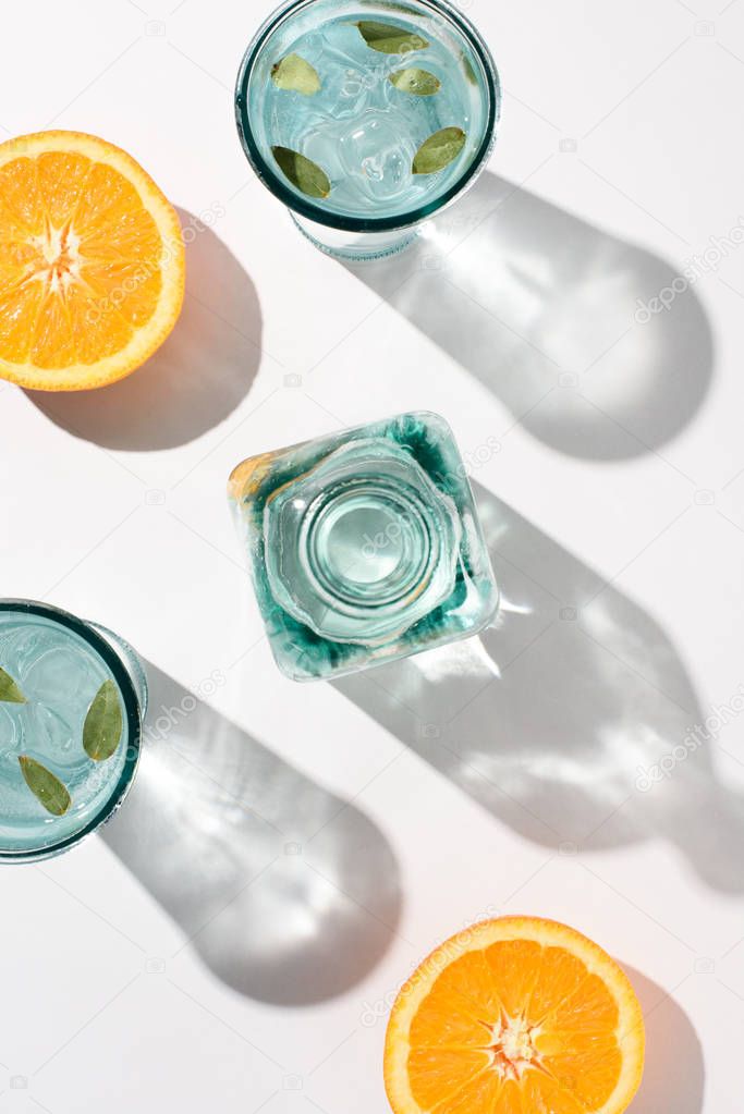 flat lay with pieces of orange, bottle and glasses with water and ice on white surface