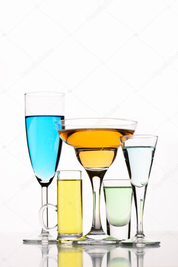 close up view of various alcohol cocktails in glasses on white backdrop