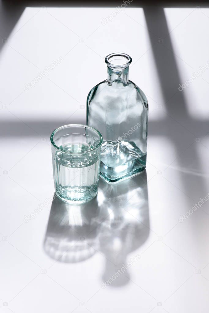 close up view of glass and bottle with water on white surface