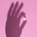 Vista superior da sombra da mão segurando pílula na superfície rosa
