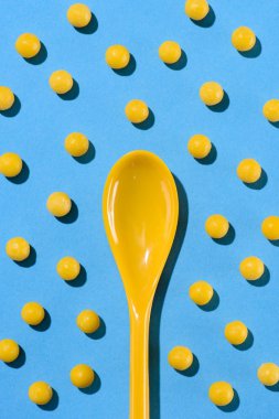 top view of yellow plastic spoon surrounded with pills on blue clipart