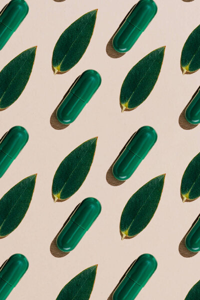 top view of phytotherapy pills with green leaves in rows pattern on beige surface
