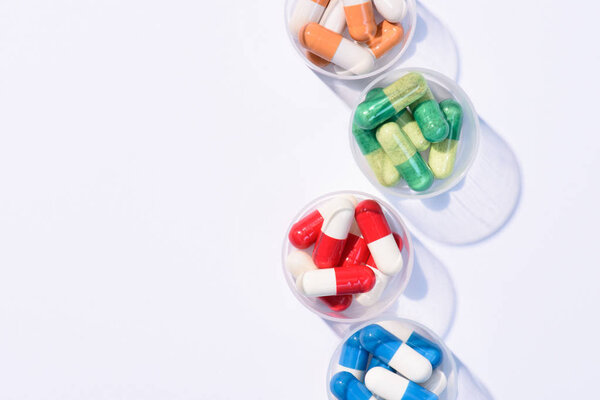 top view of various colorful pills in plastic bowls on white