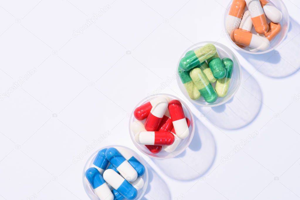 top view of various colorful pills in plastic bowls in row on white