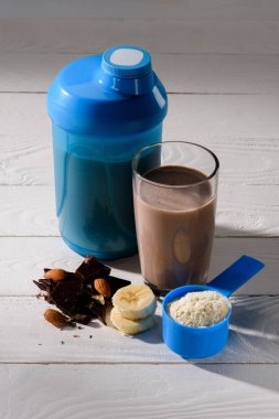 Shaker ve protein içeceği badem, muz ve çikolata Beyaz ahşap masa üzerinde bardak
