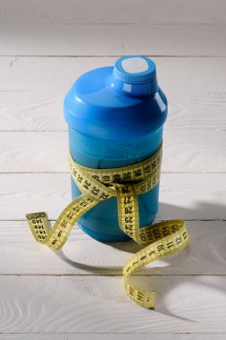 close-up shot of protein shaker tied with measuring tape on white wooden table clipart