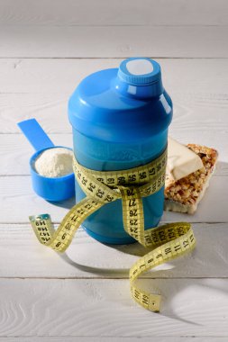 close-up shot of protein shaker tied with measuring tape and energy bars on white wooden table clipart