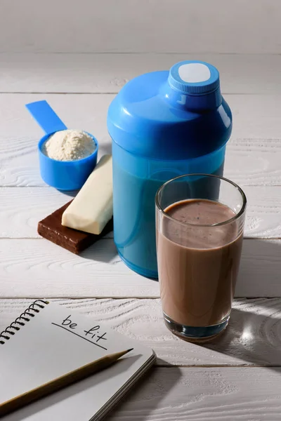 Schokoladenproteinshake Mit Energieriegeln Und Notizbuch Mit Fitnessschild Auf Weißem Holztisch — Stockfoto
