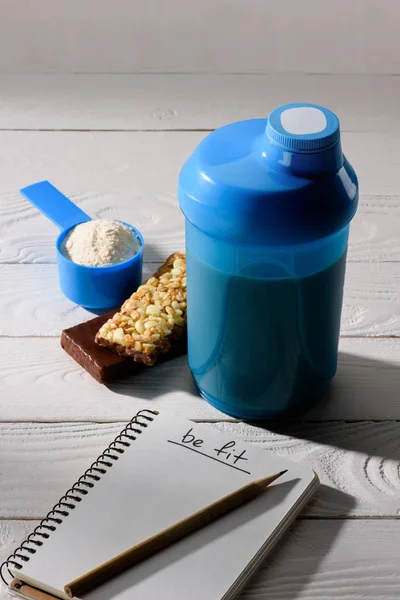 protein shaker with energy bars and measuring tape on white wooden table