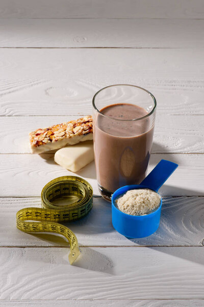 chocolate protein shake with energy bars and measuring tape on white wooden table