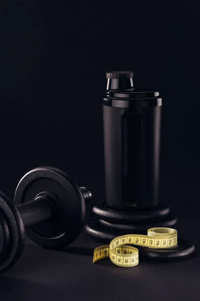 protein shaker with dumbbell and measuring tape isolated on black