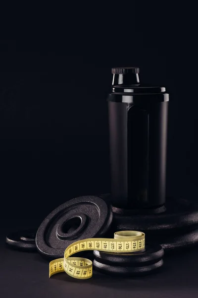 protein shaker with measuring tape and weight plates isolated on black