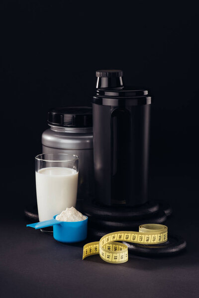 protein shaker with glass of white liquid and measuring tape isolated on black