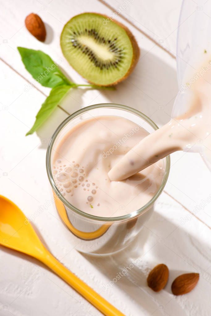 high angle view of protein drink pouring into glass on white wooden table with half of kiwi