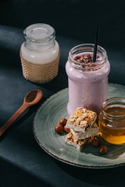 berry yüzlü içme ile saman, dilim enerji bar, reçel ve ceviz closeup görünümünü tabak, kaşık ve yoğurt masada şişe 