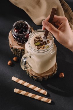 cropped image of female mixing milkshake by spoon, currants, sweet straws and walnuts  clipart
