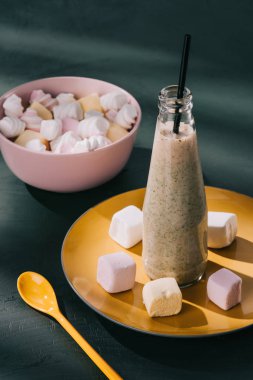 closeup shot of milkshake in bottle with drinking straw, bowl with marshmallows and spoon on tabletop clipart