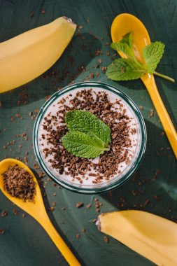 top view of milkshake with chocolate shavings and mint, spoons and bananas on table clipart