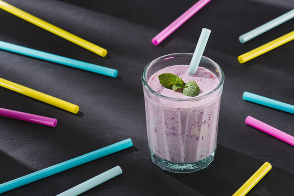 closeup image of drinking straws and glass of berry smoothie with mint 