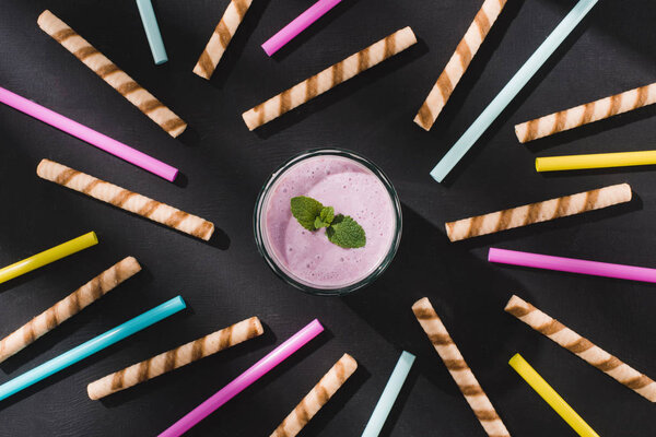 top view of berry smoothie with mint surrounded by drinking straws and sweet straws on table 