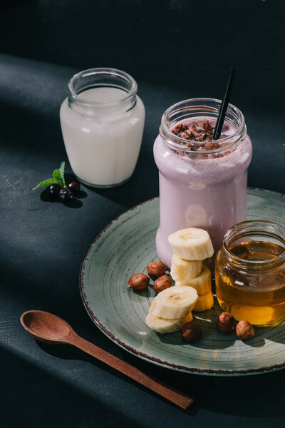 closeup image of berry smoothie, jam, banana slices and walnuts on plate, spoon, yogurt and currants 