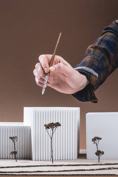 частичный вид архитектора с кистью и строительной моделью на коричневом фоне
