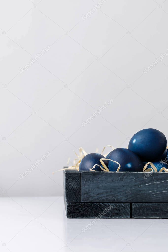 blue Easter eggs in wooden box on white surface isolated on grey