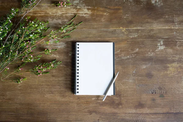 Top view of notepad with pencil and flowers on wooden tabletop — Stock Photo