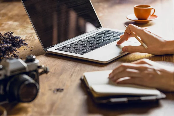 Personne utilisant un ordinateur portable et un journal à l'espace de travail avec un appareil photo vintage — Photo de stock