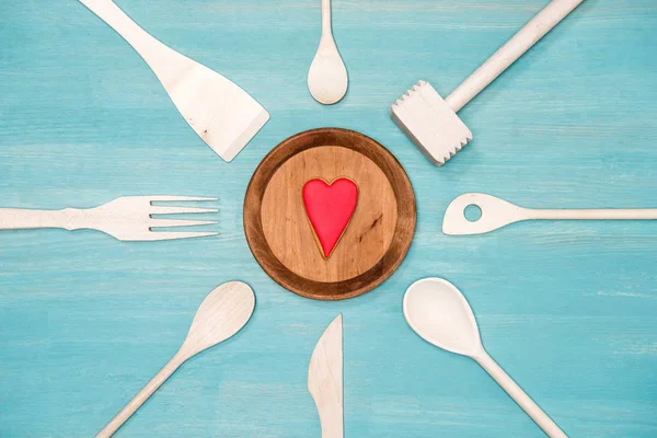 Vista dall'alto di vari utensili da cucina in legno con simbolo del cuore sul piatto — Foto stock