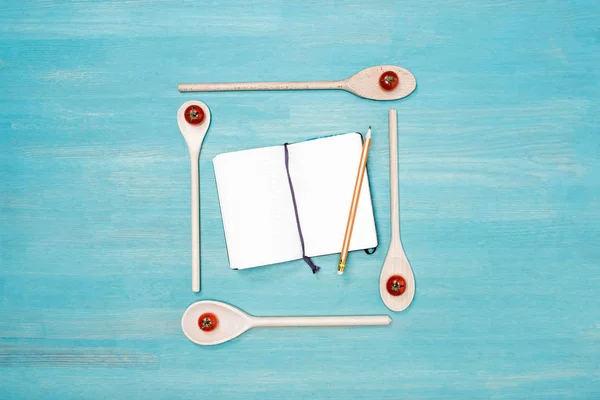 Top view of wooden spoons with cherry tomatoes and blank open cookbook with pencil on table — Stock Photo