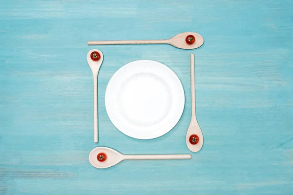 Vista superior de cucharas de madera con tomates cherry y plato blanco vacío en la mesa - foto de stock