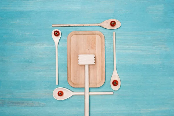 Top view of wooden cutting board, meat hammer and spoons with cherry tomatoes on table — Stock Photo