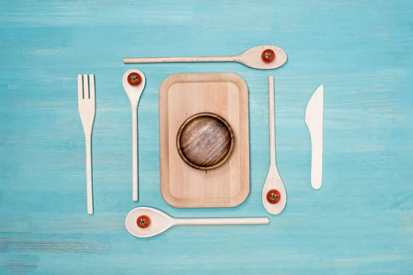 Vista superior da placa de corte de madeira com utensílios de cozinha e tomate cereja na mesa — Fotografia de Stock