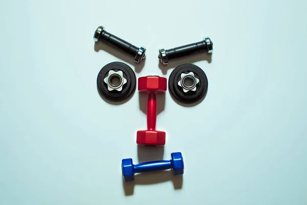 Top view of various dumbbells and weight plates in shape of serious face — Stock Photo