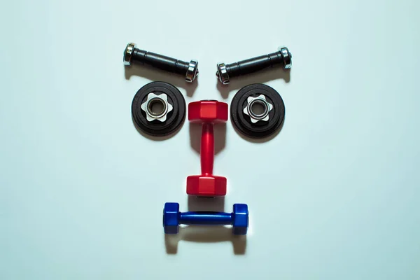 Top view of various dumbbells and weight plates in shape of serious face — Stock Photo