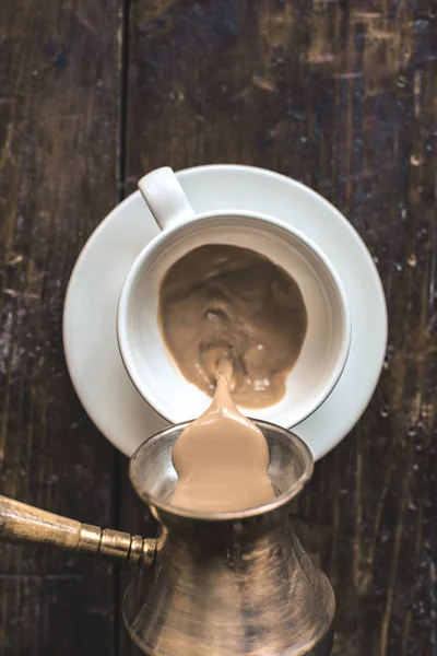 Наливая кофе из cezve в чашку на стол — стоковое фото