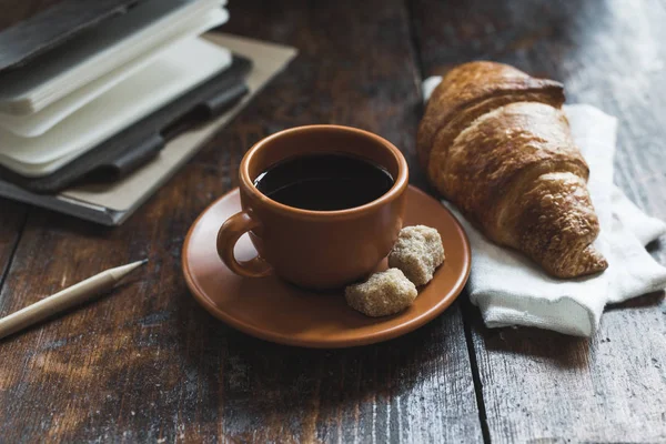 Kaffee mit Croissant und Notizbücher mit Bleistift auf Tischplatte — Stockfoto