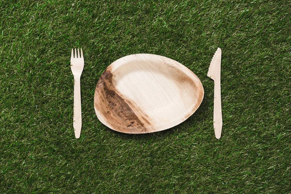 Деревянная тарелка с вилкой и ножом на траве — стоковое фото