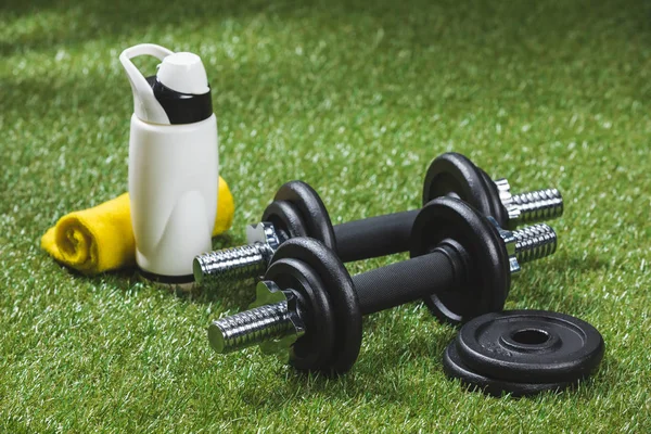 Dumbbells and bottle of water with towel on grass — Stock Photo