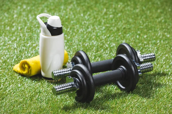 Dumbbells and bottle of water with towel on grass — Stock Photo