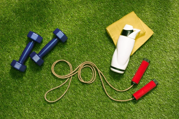 Haltères et bouteille avec corde à sauter sur l'herbe — Photo de stock