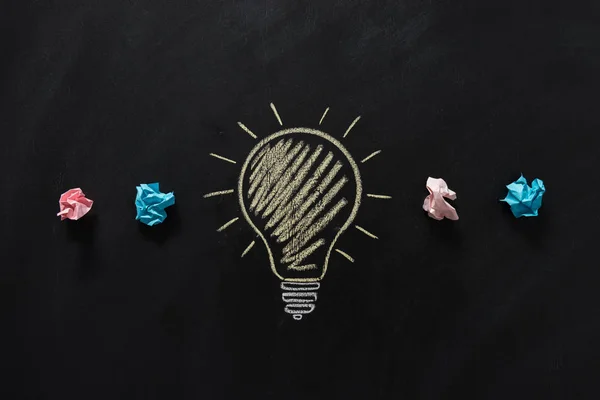 Paper rubbish with electric bulb on blackboard — Stock Photo