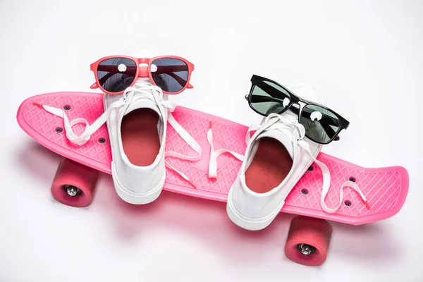 Sneakers and sunglasses on skateboard — Stock Photo