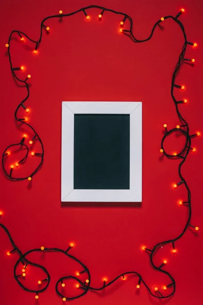 Top view of empty frame and christmas lights isolated on red — Stock Photo